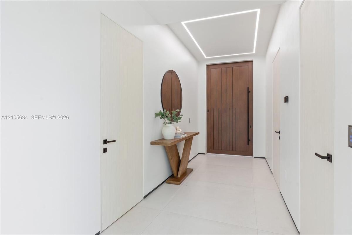 Entryway featuring a large-format wood-finish front door with a vertical pull handle, recessed linear ceiling lighting, minimalist flat-panel interior