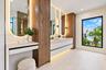 Floating double vanity with integrated wood-finish cabinetry, arched mirrors with perimeter lighting, stone-top surfaces, and matte black fixtures