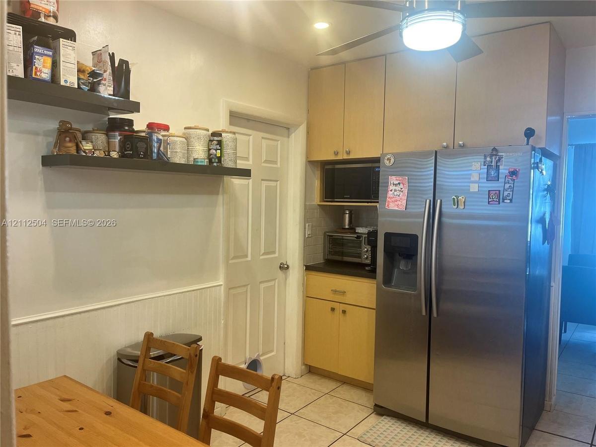 Kitchen area featuring light-finish cabinetry, stainless steel side-by-side refrigerator, floating shelving, white wainscoting, and ceramic tile floor