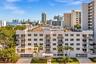 Mid-rise residential building featuring white stucco facade, multiple private balconies with railings, and mature palm tree landscaping