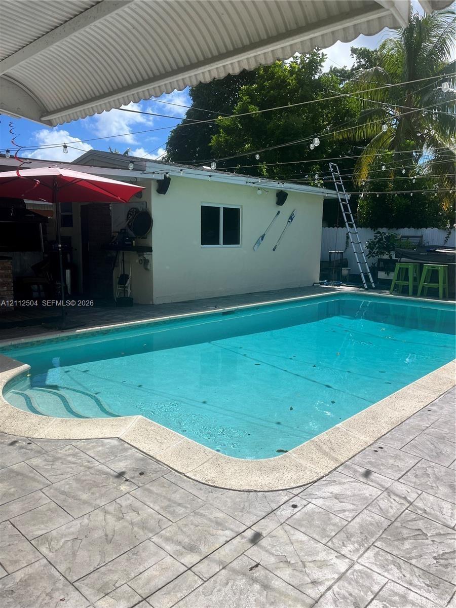 In-ground swimming pool with integrated entry steps, concrete pool decking, and overhead covered patio structure
