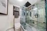 Walk-in shower with stone-tile surround, glass enclosure, and rainfall showerhead, complemented by a matte black heated towel rail and wall-mounted pl