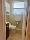 Restroom featuring wood-finish flooring, a contemporary dark-finish vanity, a white high-profile toilet, white built-in wall cabinetry, and an opaque 
