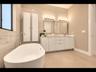 Luxurious primary bath with a freestanding soaking tub, dual-sink vanity, custom white cabinetry, and floor-to-ceiling tile