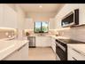 Modern kitchen with crisp white cabinetry, stone countertops, full-height stone backsplash, under-cabinet lighting, and stainless steel appliances