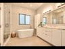 Spa-inspired primary bath with a freestanding soaking tub, glass walk-in shower, double vanity, and full-width illuminated mirror