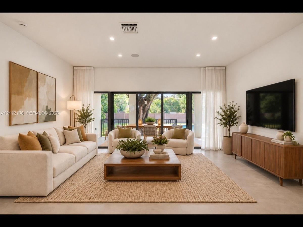 Bright living area with large-format tile, recessed lighting, and multi-panel sliding glass doors that open to the covered patio for seamless indoor-o