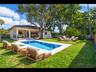 Resort-style backyard with an in-ground pool, stone paver deck, covered patio, and mature trees for natural shade and privacy