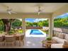 Spacious covered patio with stone-look tile and ceiling fans, overlooking the rectangular pool — ideal for entertaining or relaxing in the shade
