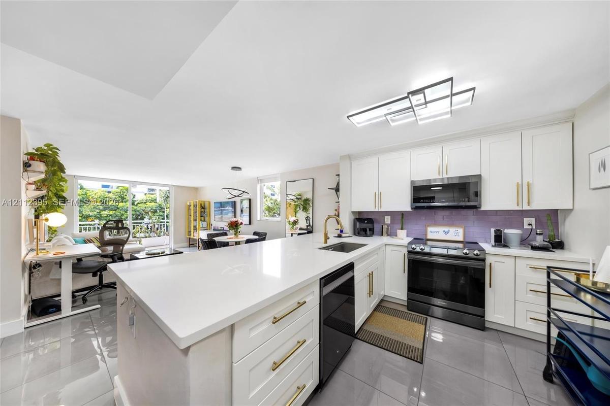 Kitchen featuring a central island with a quartz countertop, white shaker-style cabinetry with gold-tone pulls, a purple tile backsplash, large-format