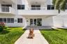 Multi-story residential building exterior featuring a covered entryway, dual glass-panel entrance doors, second-level balconies with white railings, a