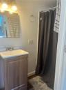 Bathroom featuring a wood-finish vanity with a rectangular sink, chrome dual-handle faucet, rectangular wall-mounted mirror, and tiled shower surround