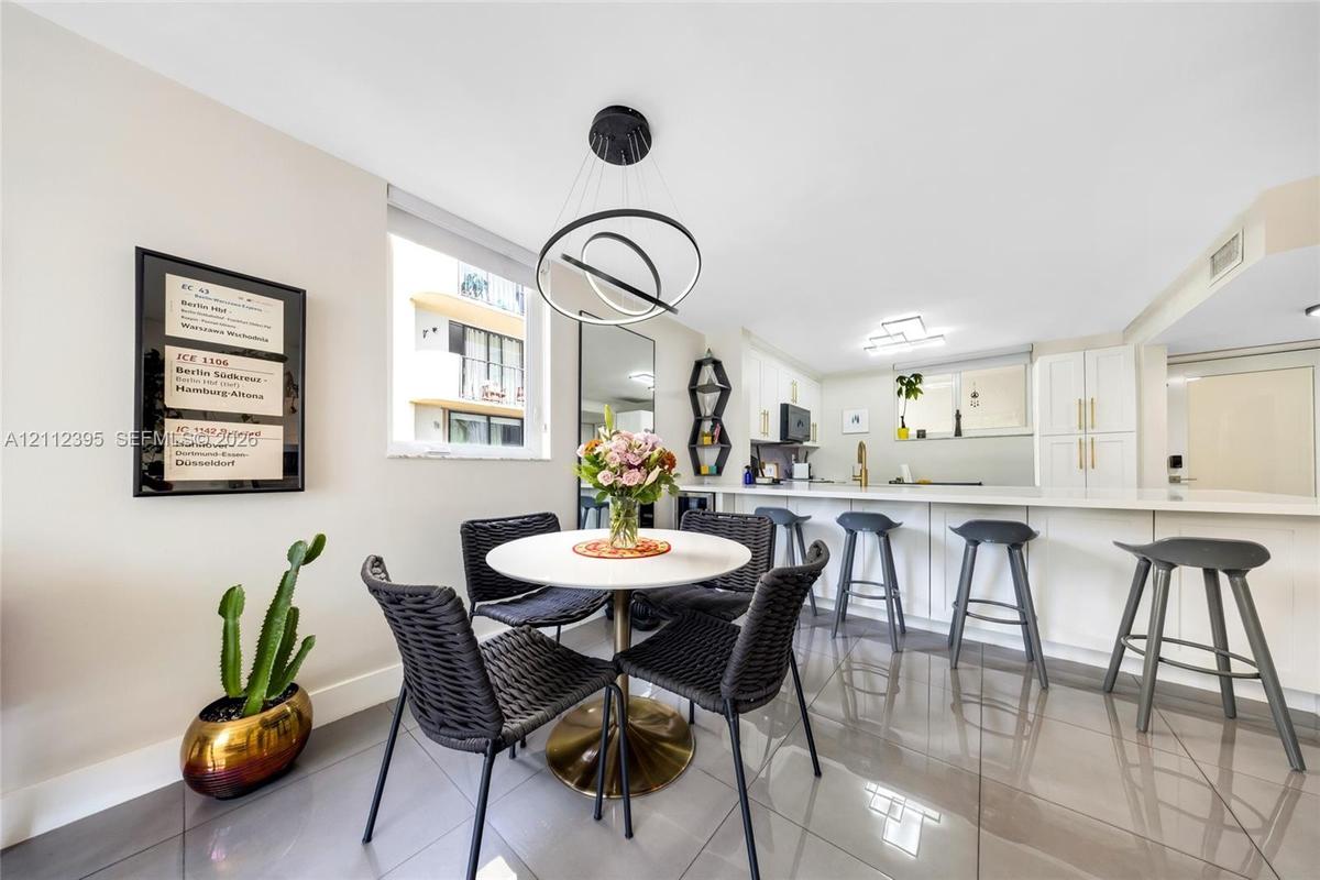 Open-concept kitchen and dining area featuring large-format tile flooring, white cabinetry with gold-tone hardware, a breakfast bar, and a modern tier