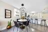 Open-concept kitchen and dining area featuring large-format tile flooring, white cabinetry with gold-tone hardware, a breakfast bar, and a modern tier