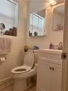 White vanity cabinet with an integrated sink and metal faucet, tri-fold mirrored medicine cabinet, and ceramic tile flooring