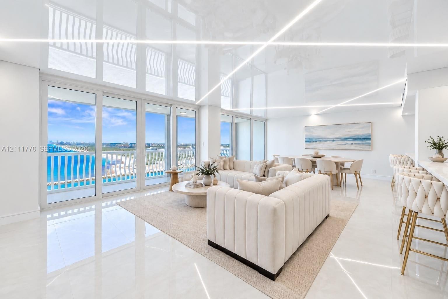 High-gloss ceiling with integrated linear lighting, large-format tile flooring, and expansive floor-to-ceiling glass sliding doors opening to a balcon