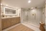 Dual vanity with wood-finish cabinetry, quartz countertops, integrated LED-backlit mirror, and gold-toned fixtures