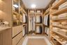Walk-in closet featuring custom wood-finish cabinetry, integrated linear LED shelving illumination, gold-tone metal hardware, and glass-front display 