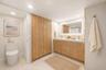 Bathroom featuring a wood-finish double vanity with dual gold-toned faucets, integrated solid-surface countertop, full-width illuminated vanity mirror