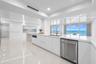 Modern kitchen featuring sleek white cabinetry, stone-finish countertops, stainless steel appliances, and large-format tile flooring, complete with ex