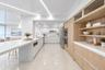 Contemporary kitchen featuring a sprawling waterfall-edge island, high-gloss flat-panel cabinetry, light-toned wood-finish cabinetry accents, integrat