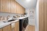 Laundry room featuring floor-to-ceiling wood-finish cabinetry, a drop-in stainless steel sink, a gold-toned gooseneck faucet, and white countertops