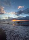 Oceanfront setting featuring direct water access, sandy beach terrain, and a horizon sunset