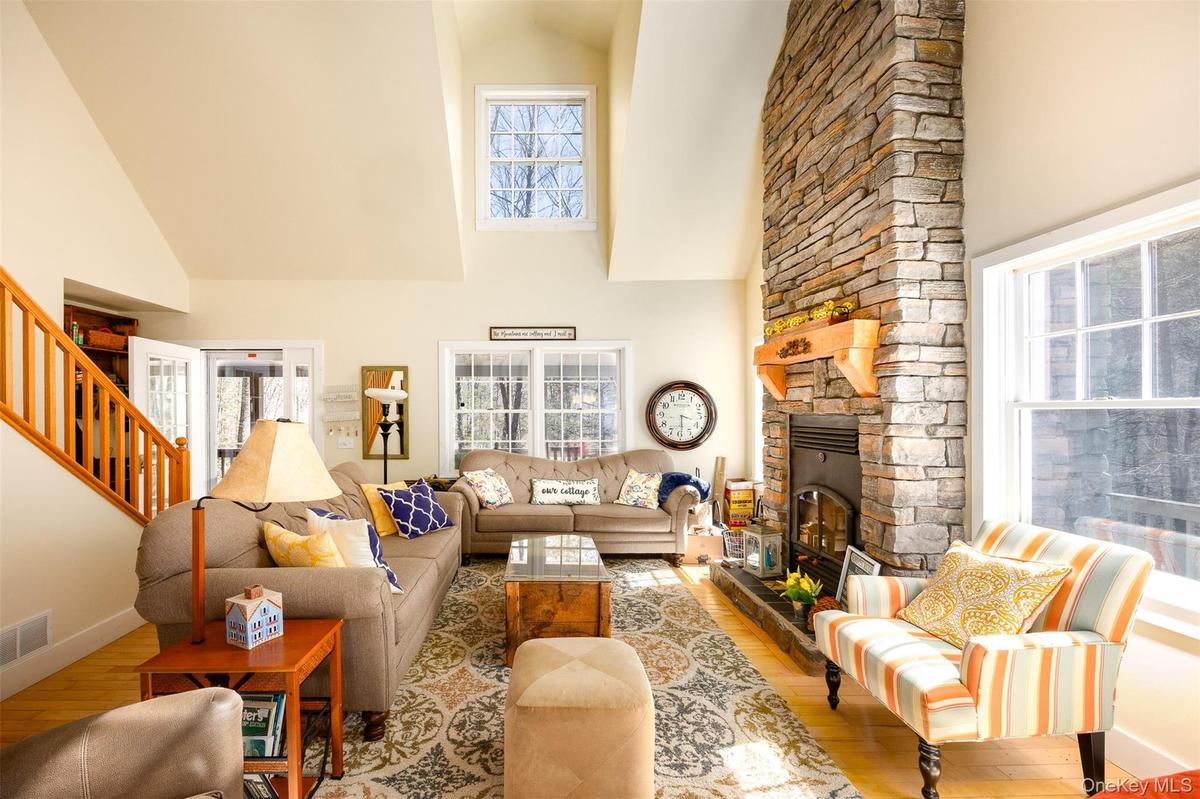 Living room with hardwood / wood-style flooring, a stone fireplace, and a high ceiling