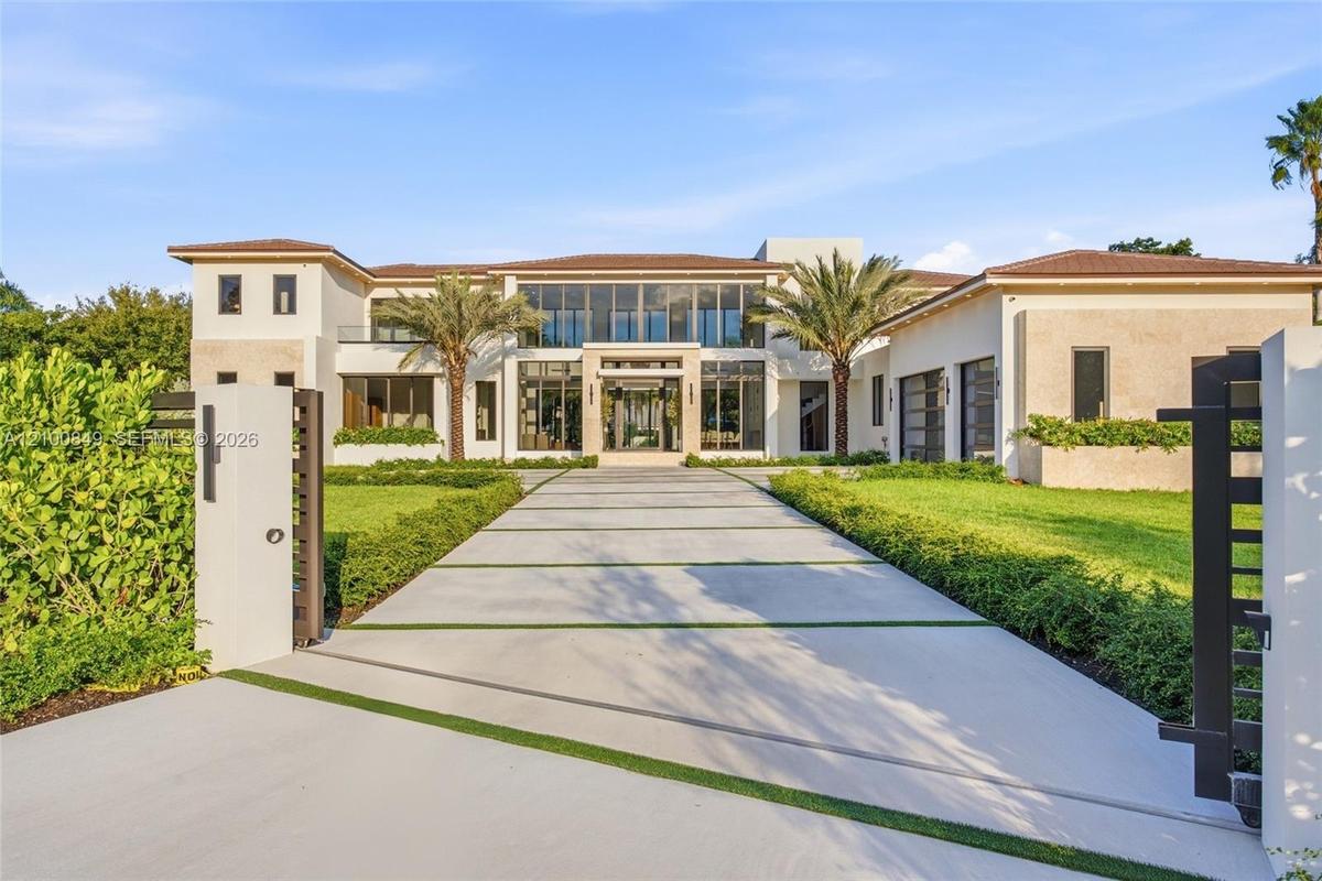 Modern estate featuring a structured concrete driveway with turf ribbons, a multi-story facade with expansive floor-to-ceiling glass paneling, tile ro