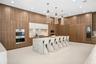 Floor-to-ceiling cabinetry, stone-clad waterfall island, built-in stainless steel double oven, integrated refrigeration, and three sculptural pendant 