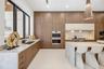 Kitchen featuring flat-panel wood-finish cabinetry, stone countertops with waterfall edge, integrated stainless steel double wall oven, and geometric 