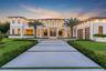 Modern two-story estate featuring a smooth stucco finish, extensive floor-to-ceiling glass wall facade, paved driveway with geometric grass inlay, til