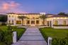 Two-story modern residence featuring stone-clad exterior walls, expansive floor-to-ceiling glass windows, a structured concrete paver driveway, and pr