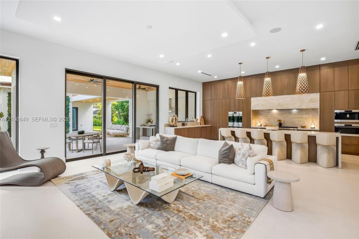 Open-concept space featuring floor-to-ceiling wood-finish cabinetry, a large kitchen island with waterfall-edge countertop, recessed lighting, and mul