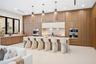 Full-height wood-finish cabinetry, waterfall-edge island with light-toned countertop, integrated stainless steel appliances, recessed lighting, and th