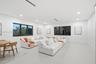 Open-concept interior featuring smooth white flooring, recessed ceiling lighting, linear ceiling vents, and large-format windows with dark frames