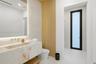 Floating stone vanity with integrated basin, wall-mounted brass faucet, illuminated recessed mirror, and wood-panel accent wall