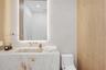 Stone-clad integrated vanity with a seamless basin, wall-mounted faucet, backlit rounded mirror, and wood-finish wall paneling