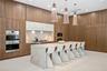 Custom floor-to-ceiling wood cabinetry, expansive stone-topped kitchen island, dual built-in ovens, stone slab backsplash, and three architectural pen