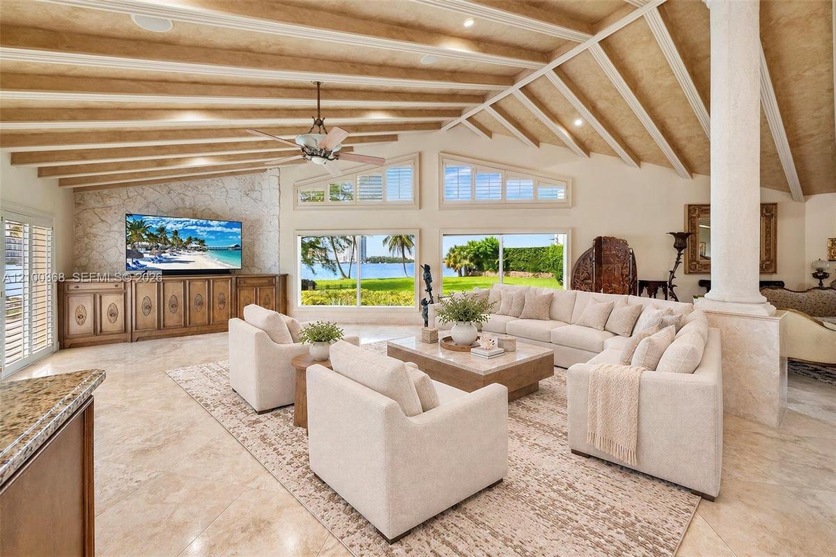 Vaulted beamed ceiling featuring recessed lighting, stone-textured accent wall with integrated cabinetry, polished stone flooring, and expansive windo