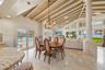 Open-concept living space featuring vaulted ceilings with exposed wood beams, natural stone flooring, a decorative stone column, and expansive floor-t