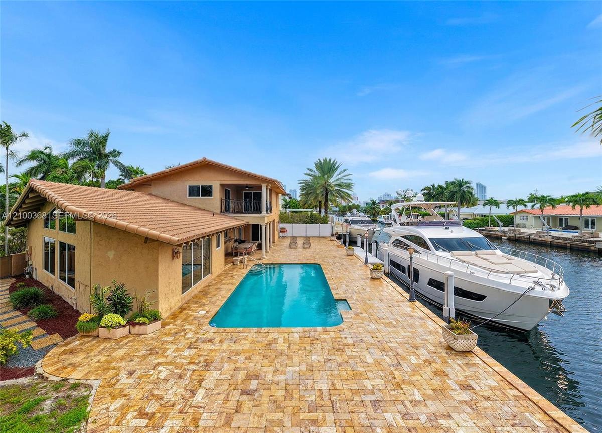 Waterfront residence featuring a private boat dock, in-ground swimming pool, expansive stone-paver patio, and two-story stucco exterior with a tile ro