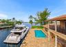 Waterfront estate featuring a private boat slip, rectangular swimming pool, stone-paver patio, covered porch with classical columns, and an upper-leve