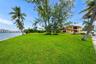 Expansive waterfront property featuring a manicured lawn, mature trees, palm trees, and direct water frontage