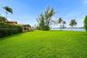 Expansive waterfront lawn featuring manicured turf, mature palm trees, and direct water frontage