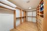 Walk-in closet featuring custom wood cabinetry, extensive shelving, hanging rods, integrated drawer units, and wood-finish flooring
