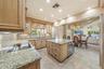 Kitchen featuring natural stone countertops, custom cabinetry, a center island with built-in wine refrigeration, tile flooring, and recessed lighting