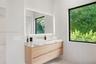 Floating wood-finish vanity with a stone countertop, wall-mounted faucet, integrated LED-backlit mirror, and large window with exterior greenery