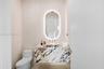 Modern powder room featuring a sculptural oval illuminated mirror with integrated lighting, elegant veined stone vanity countertop with waterfall edge