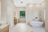Bathroom featuring a floating wood-finish double vanity, integrated stone countertop, freestanding soaking tub, glass-enclosed wet area, and recessed 
